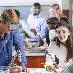 Multi-ethnic group of students in chemistry lab.  Focus on young man in blue shirt and Hispanic girl in foreground.